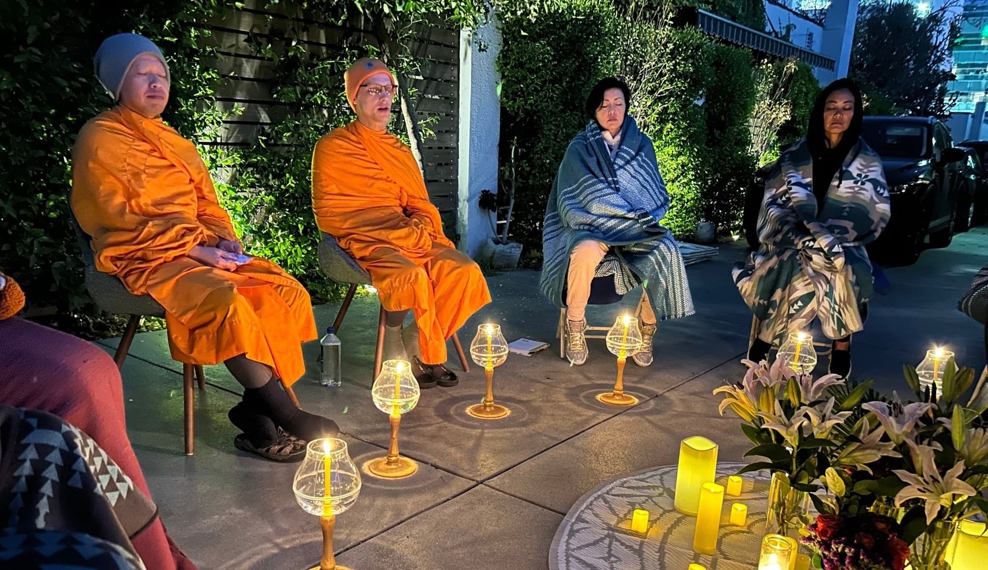 An evening candlelit gathering with monks and guests seated together outdoors.