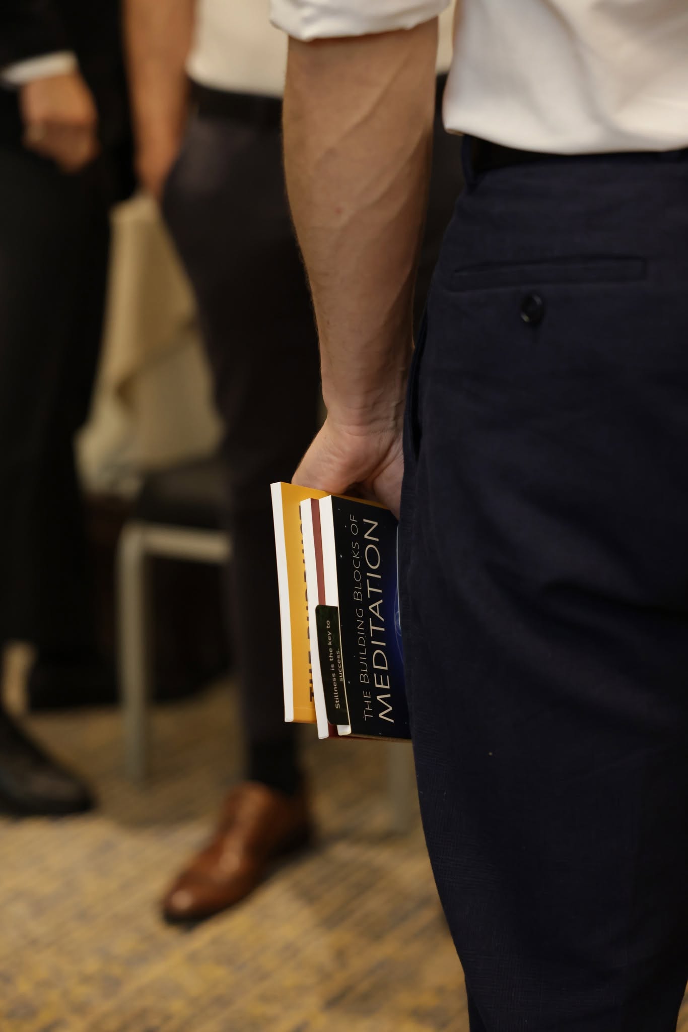 A monk in formal attire holding a stack of meditation books at an in-person engagement.